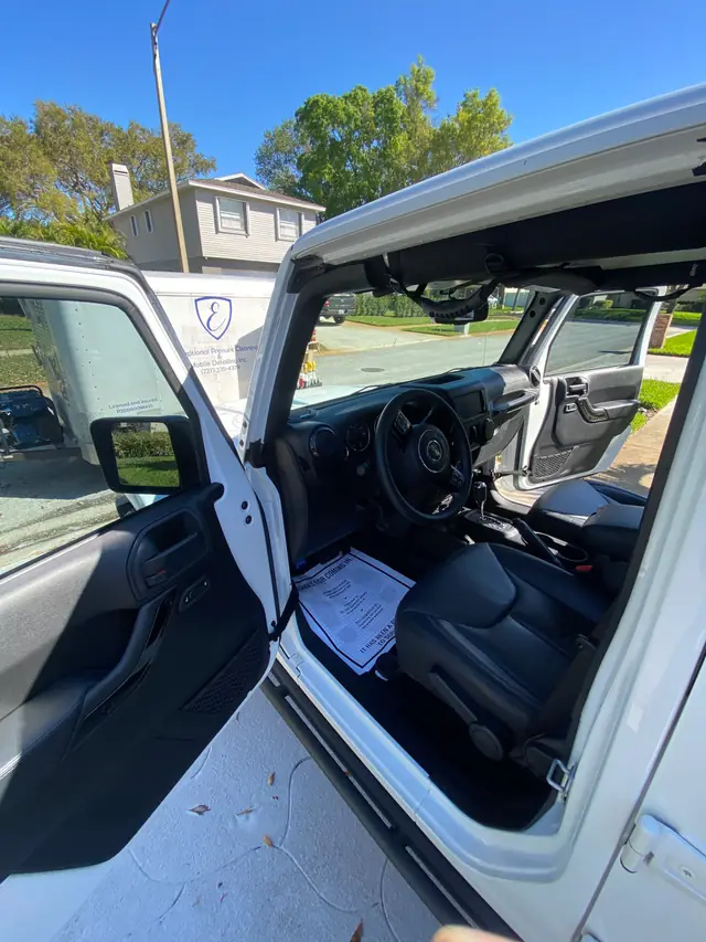 White Jeep Wrangler with its doors open on a customer's driveway, the detailing trailer parked behind