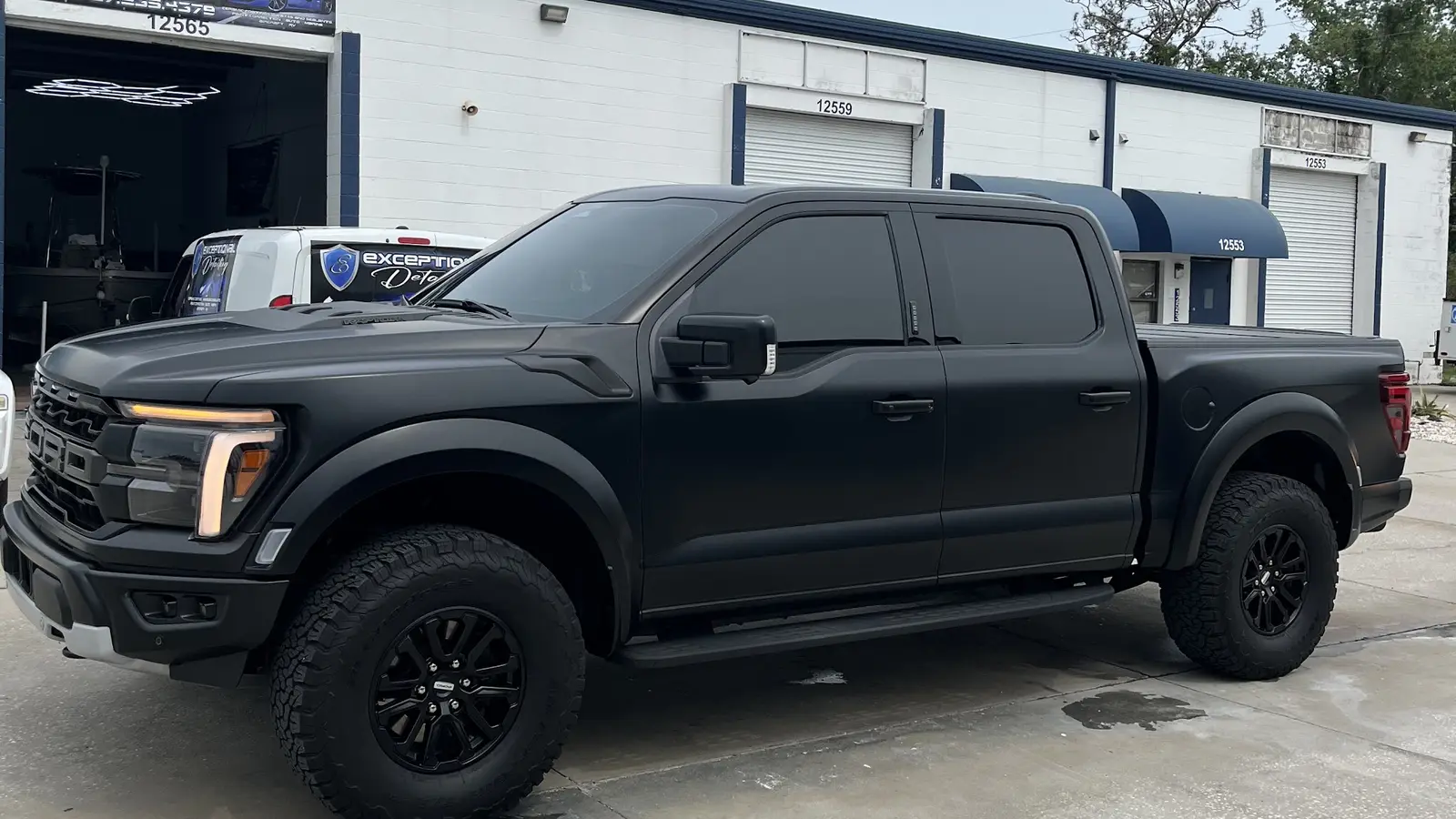 Matte-black Ford F-150 Raptor parked outside the open detail bay, the coatings van behind it
